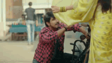 a man in a plaid shirt is kneeling down next to a woman in a yellow saree on a motorcycle .