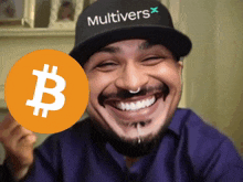 a man wearing a hat that says multivers holds up a bitcoin