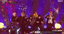 a group of people performing on a stage with a mic drop remix on the screen behind them