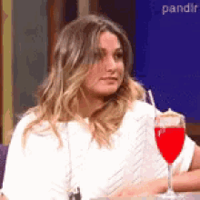 a woman is sitting at a table with a glass of red liquid in front of her .