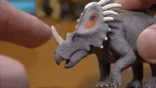 a close up of a person holding a toy dinosaur with horns .