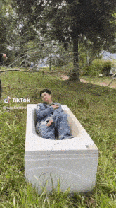 a man is laying in a bathtub in the grass with a tree in the background .