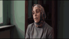 a woman wearing a hijab and a gray coat looks at the camera
