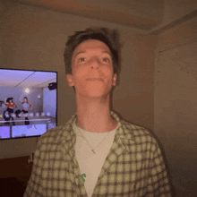 a man in a plaid shirt is standing in front of a television that shows a dance video