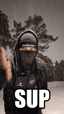 a man wearing a mask and a multiverse hat stands in the snow with the word sup above him