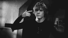 a man in a black shirt is pointing his finger at his head .