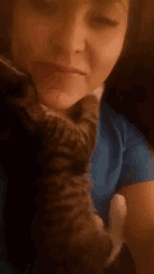 a woman in a blue shirt is holding a cat in her arms
