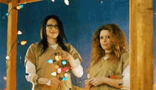 two women are standing next to each other holding a string of lights .