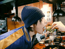 a person wearing a blue beanie and a blue jacket is eating food