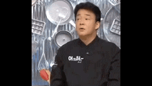 a man is sitting in front of a wall of pots and pans and making a funny face .