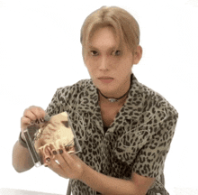 a young man wearing a leopard print shirt is holding a cd .