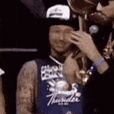 a man in a thunder jersey is talking on a cell phone while holding a trophy .
