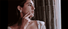 a woman wearing earrings is touching her face and looking out the window