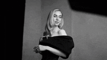 a black and white photo of a woman in a black dress looking at the camera .