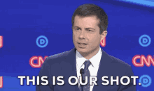 a man in a suit and tie stands in front of a blue background that says this is our shot
