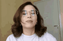 a woman wearing glasses and a white shirt making a funny face