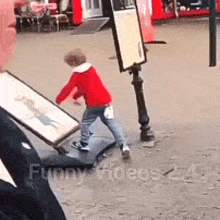 a young boy in a red jacket is standing on a sidewalk holding a picture .