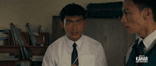 a man in a white shirt and black tie stands next to another man with kahar written on the bottom right