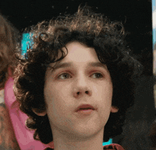 a young boy with curly hair looks at the camera with a serious look on his face