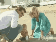 a man and a woman are kneeling on the beach with a baby