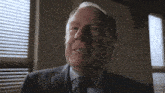 an older man in a suit and tie is smiling in front of a window