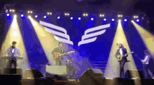 a group of people playing instruments on a stage with wings on the back