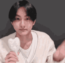 a young man in a white sweater is holding a white heart shaped object in his hands .