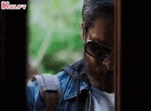 a man wearing sunglasses and a beard is standing in front of a door .