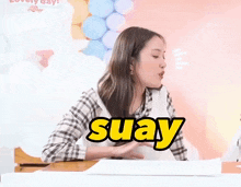 a woman is sitting at a table with the word suay on her chest
