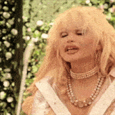 a woman with blonde hair is wearing a pearl necklace and a white shirt