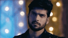 a man with a beard and mustache is looking at the camera in front of a blurry background of lights .