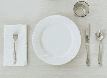 a white plate with silverware and a glass of water on a pink background