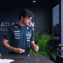 a man wearing an atlassian williams racing shirt stands in front of a window