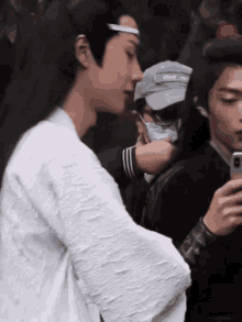 a man with long hair is taking a picture of another man with his phone .