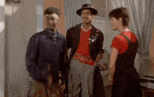 a man wearing a hat and a red shirt is standing next to two other people