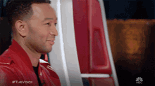 a man in a red jacket is sitting in front of a nbc logo