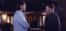 two men are standing next to each other in front of a house and talking .
