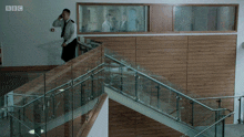 a man talking on a cell phone while walking down a set of stairs with bbc written on the wall behind him