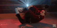 a man in a red jacket is laying on his back on a skateboard .