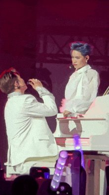a man in a white suit stands next to another man in a white suit on a stage