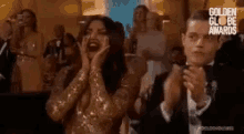 a woman in a gold dress is screaming while a man in a tuxedo is clapping .