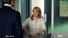 a woman in a white shirt is standing next to a man in a suit and the nbc logo can be seen in the corner