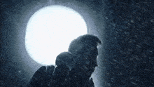 a man is singing into a microphone in the rain in front of a white light .