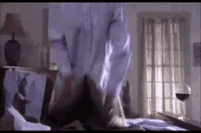 a man in a white shirt is standing on a bed in a bedroom .