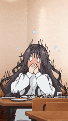 a girl with long black hair is covering her mouth with her hands while sitting at a table