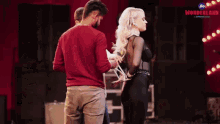 a man in a red shirt is standing next to a blonde woman in a black bodysuit .