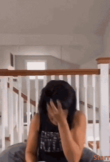 a woman in a black tank top is covering her face with her hand