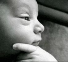 a black and white photo of a baby 's face with his hand on his chin