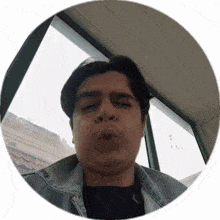 a man in a denim jacket is blowing a kiss in front of a window
