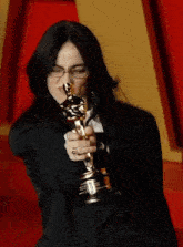 a woman in a suit holds an oscar statue in her hand